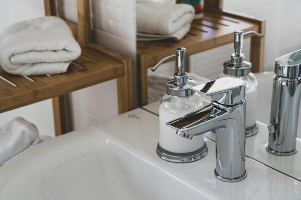 Elegant bathroom featuring a chrome faucet and soap dispenser, with a wooden shelf and plush towels.